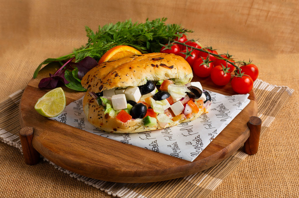 Food Village School Meals Veg Odyssey Onion Bap, black olives, cucumber, Greek cheese, tomato, onion, vinaigrette, mayo.